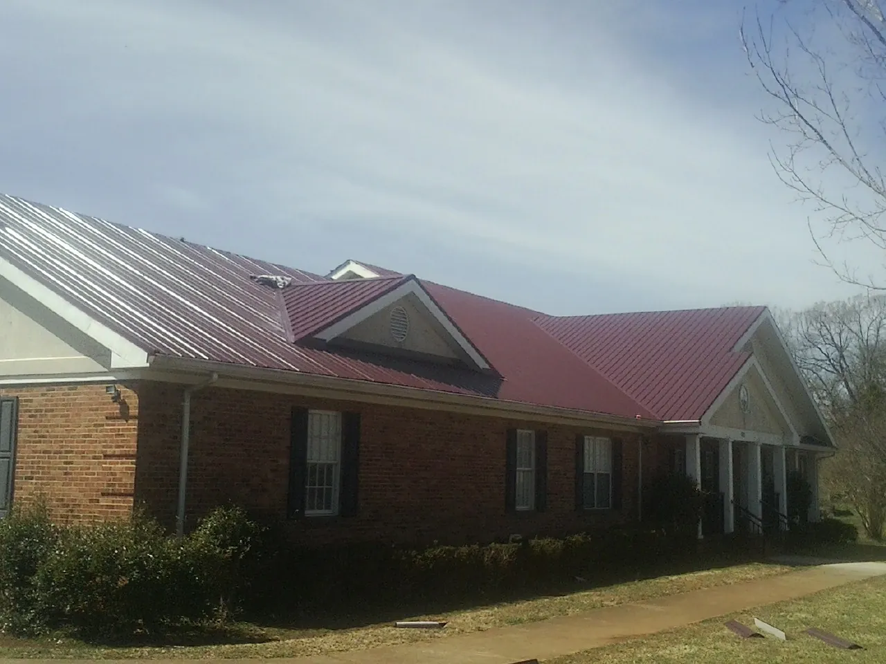 Red metal roof with gabled entries on a long brick building, from a Hail Damage Roof Repair job in Reagan