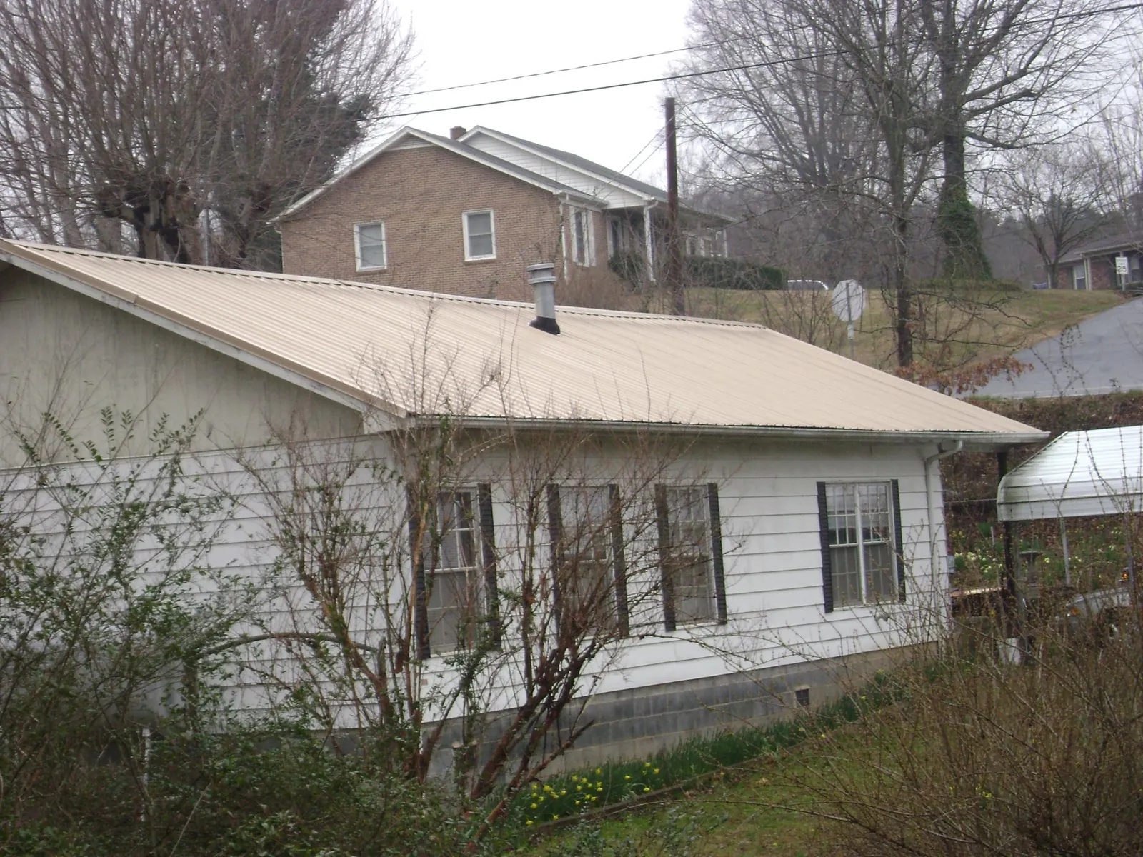 Tan metal roof on a white sided house set into a hillside — Commercial Roofing by Roofing Brothers in Reagan